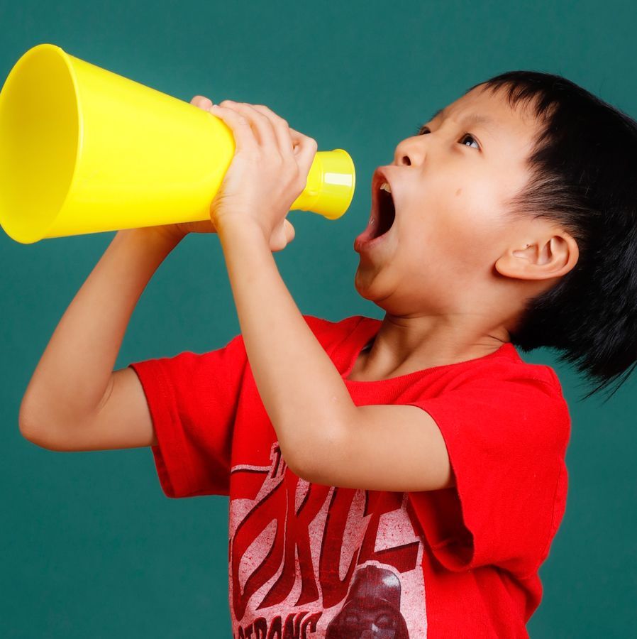 穿著紅色襯衫、張著嘴巴的小男孩在藍綠色背景下對著黃色擴音器大喊大叫。