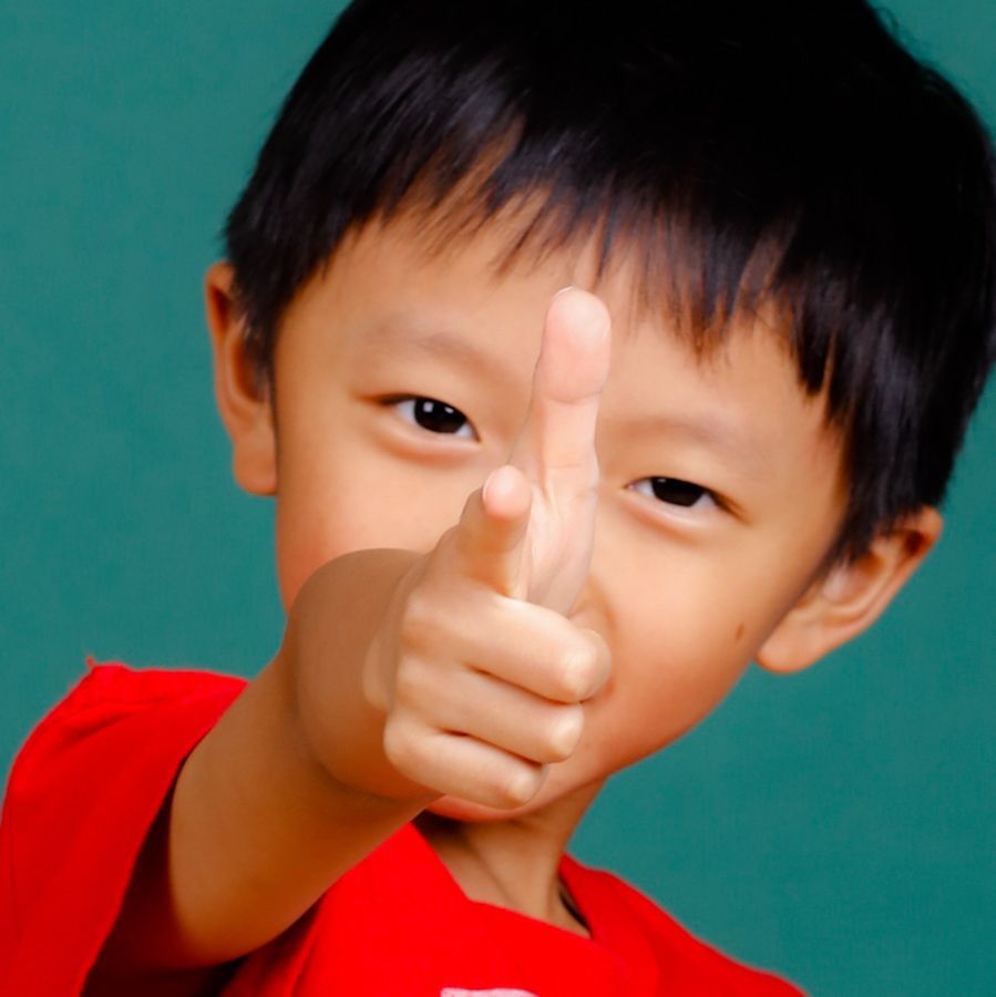 亞洲小孩用手指槍指著，表情頑皮；穿著紅襯衫。