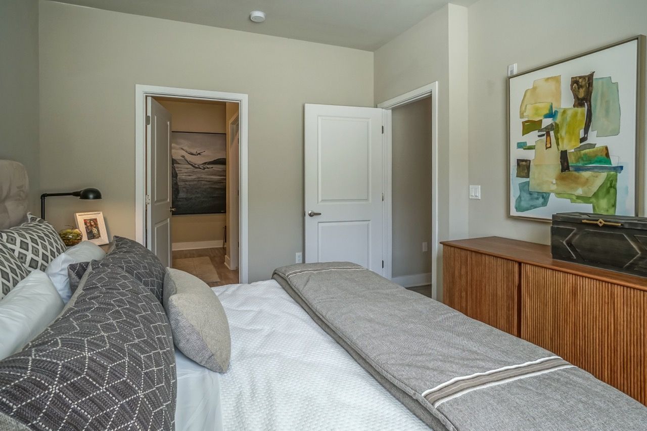 Modern apartment bedroom with a bed, pillows, dresser, abstract art, and an open door to a hallway.