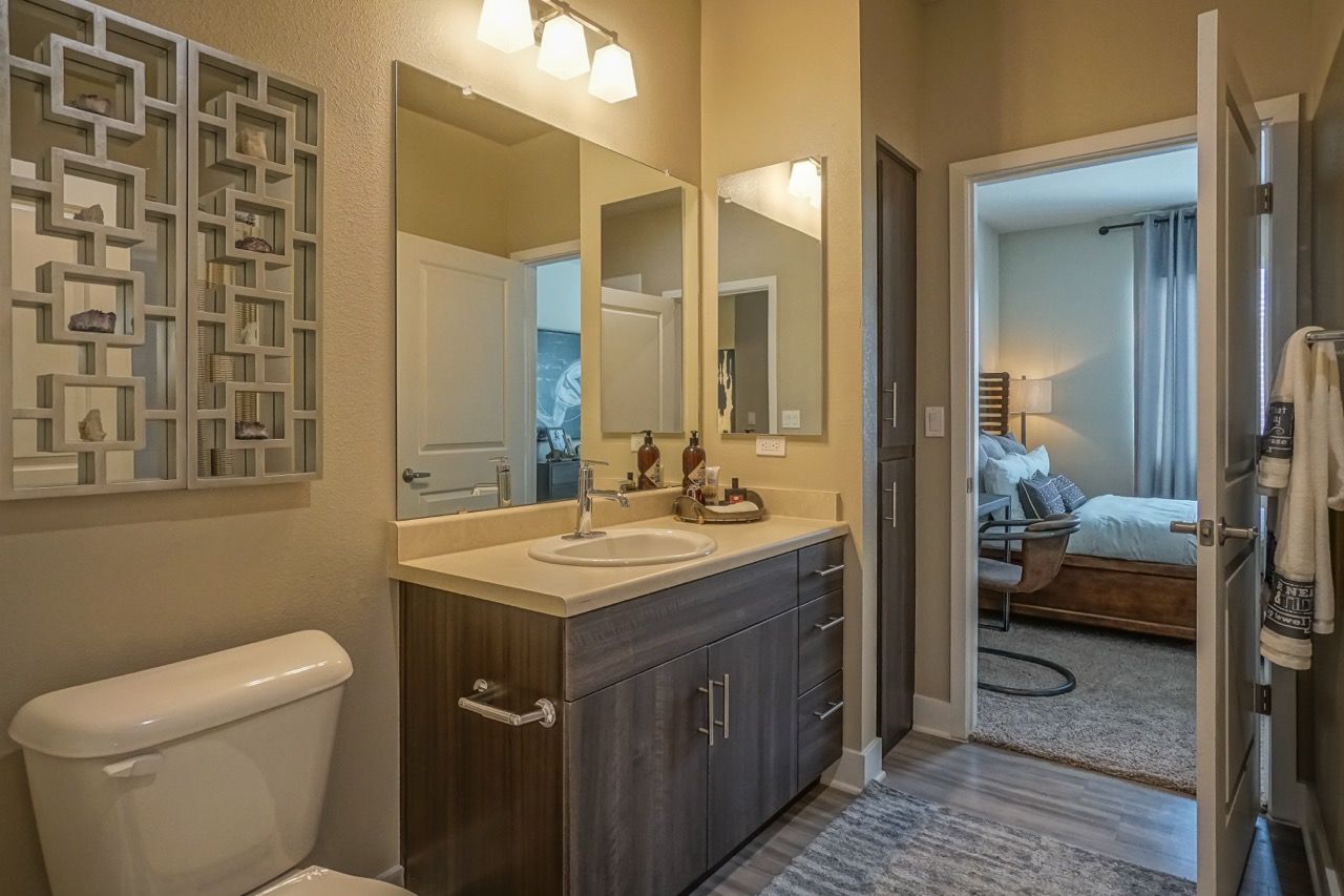 Bathroom with vanity, sink, mirror, toilet and doorway to a bedroom.