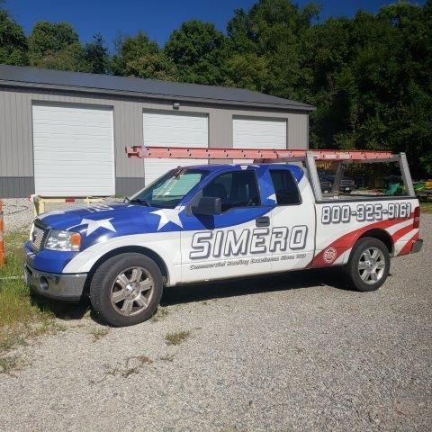 A truck with patriotic-themed graphics and company logo parked in front of a building.