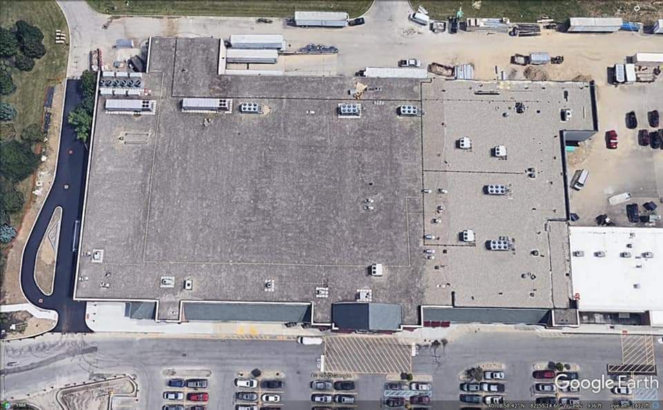 Aerial view of a large industrial building with a flat roof, surrounded by parking and roads.