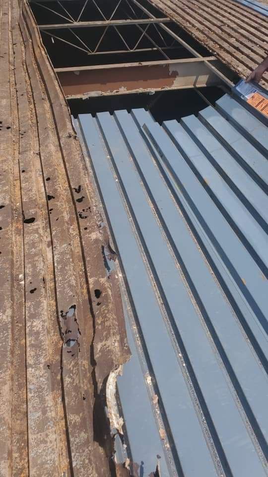 Damaged metal roof with corroded edges, a newly installed section, and an open section.