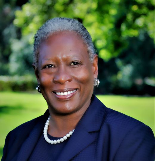 a woman wearing a blue jacket and pearls smiles for the camera
