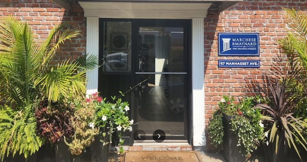 Entrance to a law firm with a brick exterior, plants, and a sign.