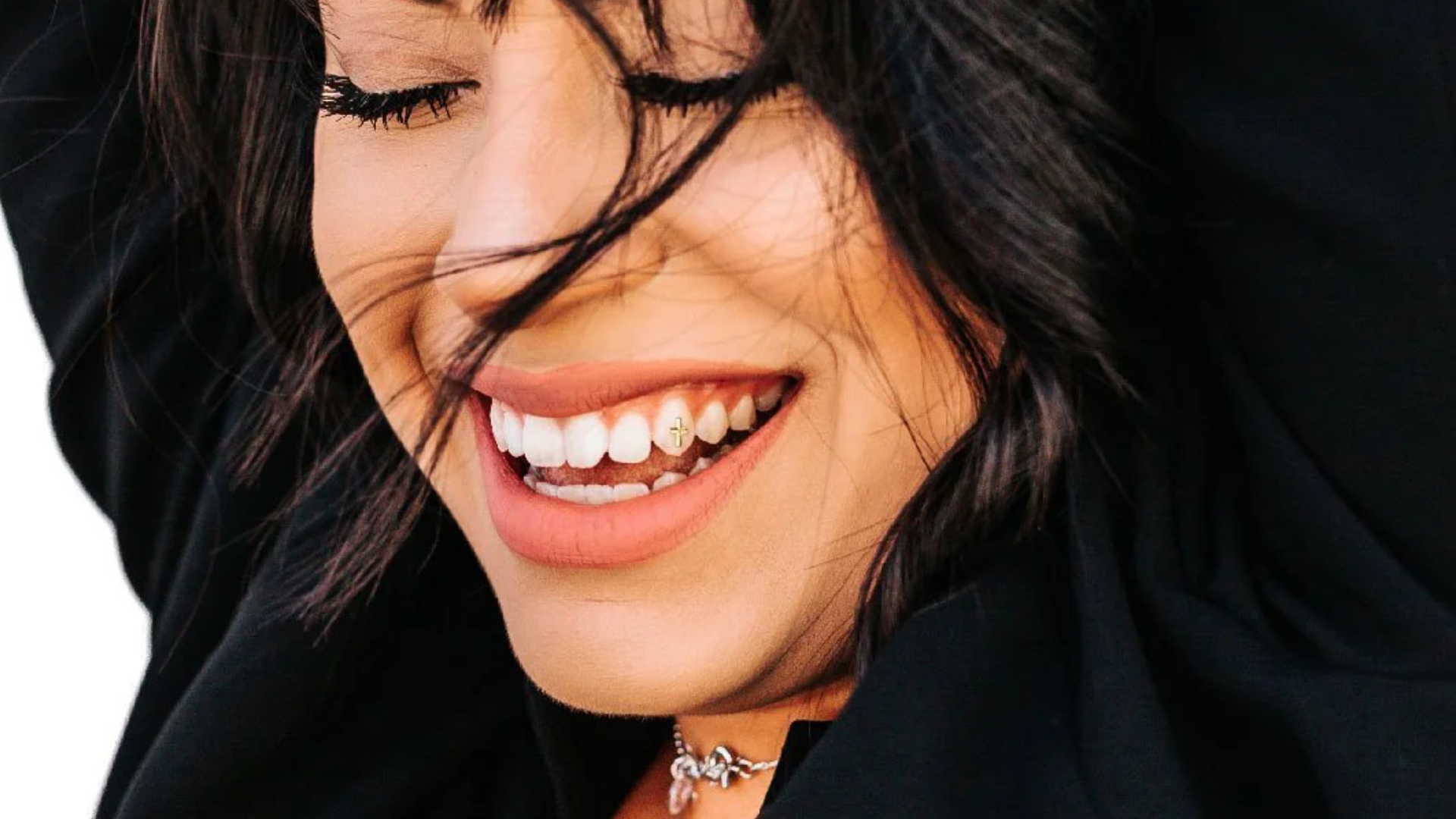 Smiling person with dark hair, eyes closed, with Twinkle on tooth  wearing black