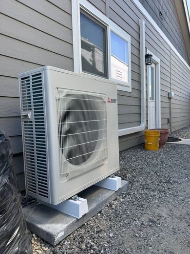 A large air conditioner is sitting outside of a house next to a window.