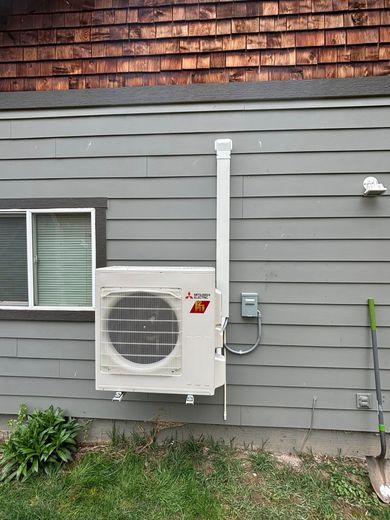 A white air conditioner is mounted on the side of a house next to a window.