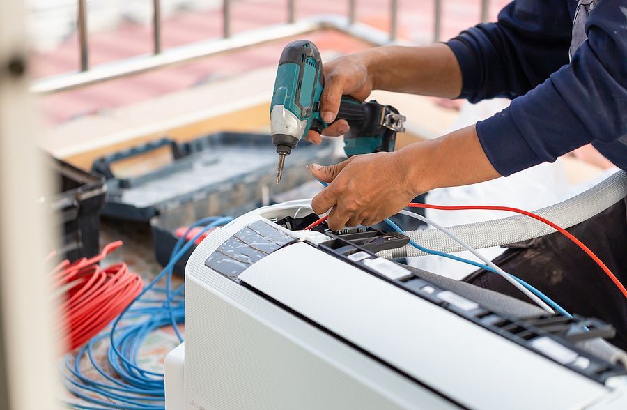 A man is fixing an air conditioner with a drill.