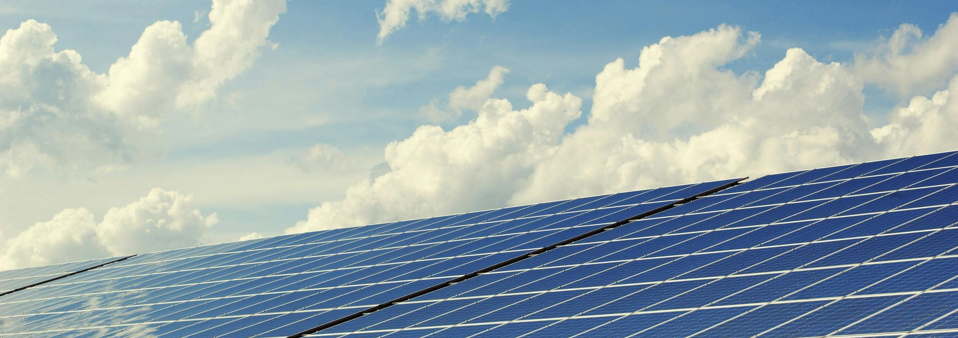 Solar panels angled toward a bright blue sky filled with white clouds.