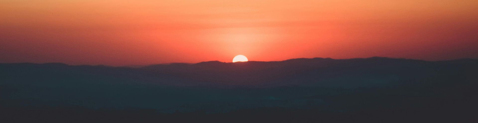 A sunset glows orange and red over a dark, silhouetted mountain range.
