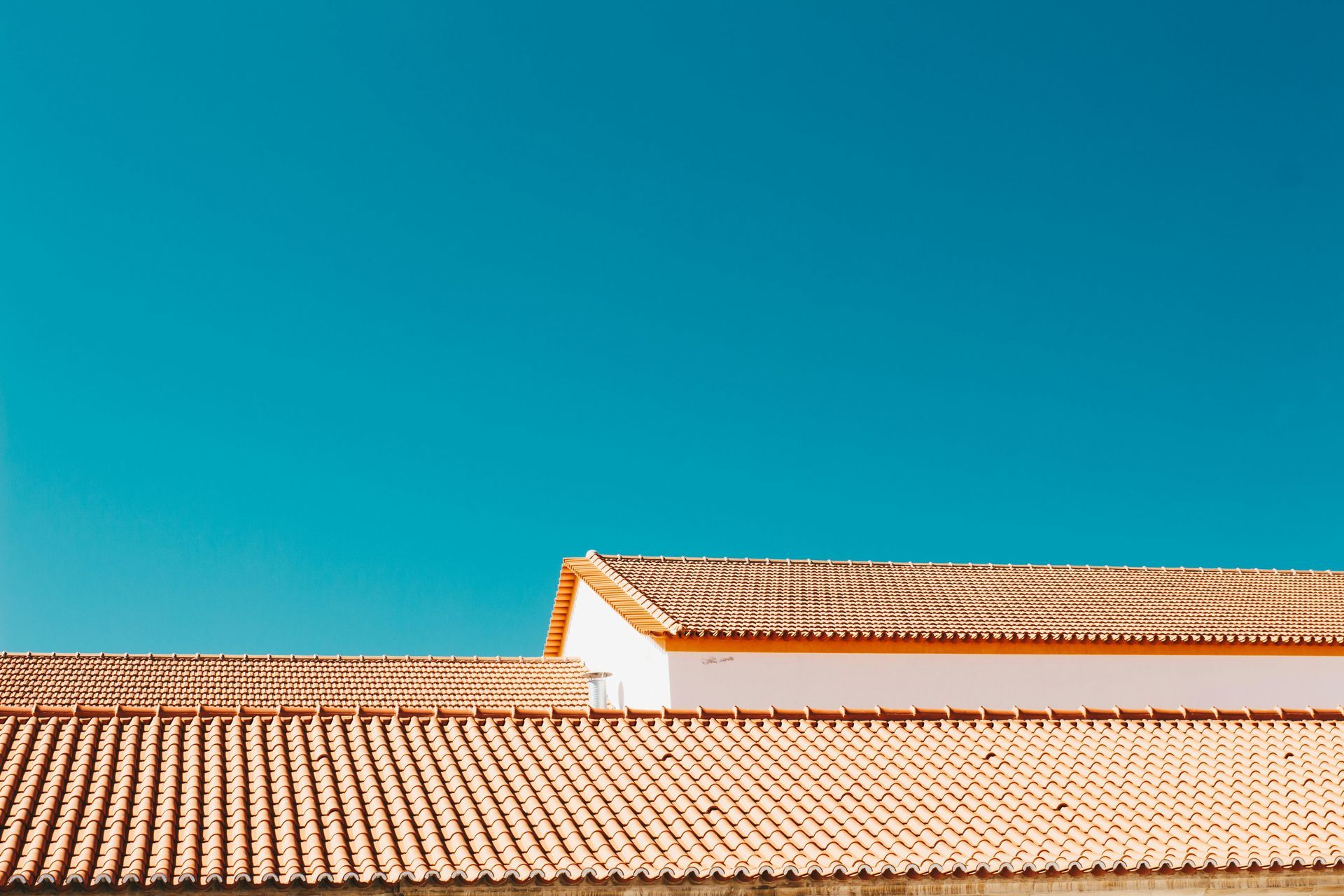 A bright blue sky above the terracotta tiled roofs of low buildings.