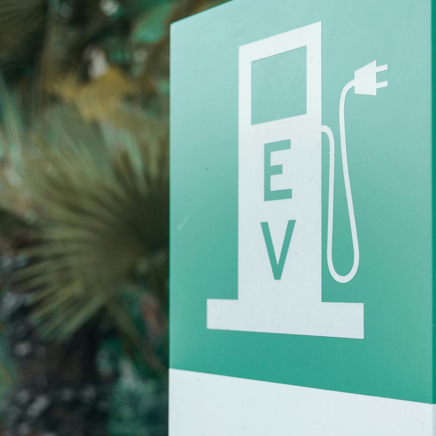 A teal green sign with a white graphic of an electric vehicle charging station and the letters
