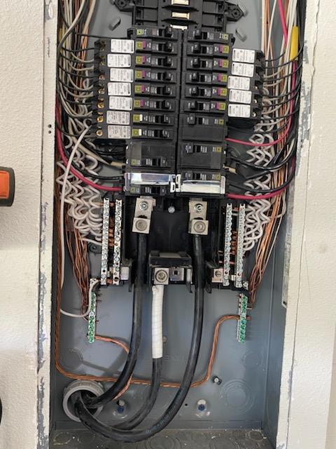 Electrical panel with numerous wires and breakers. Black and copper wires, metal box.