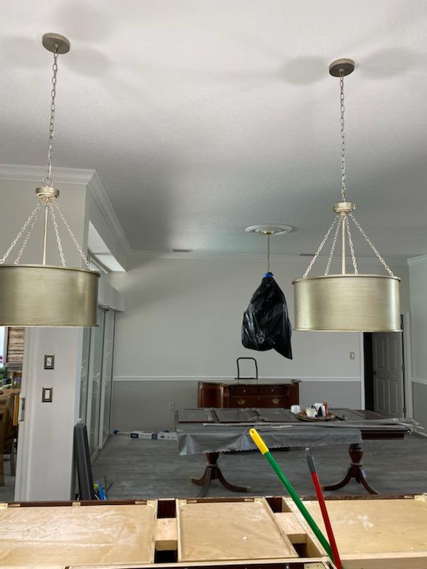 Two drum pendant lights hang from a white ceiling; a dining room with a table covered in a cloth is visible.