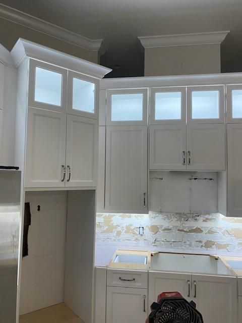 White kitchen cabinets under construction; corner unit with glass doors, lower cabinets visible.