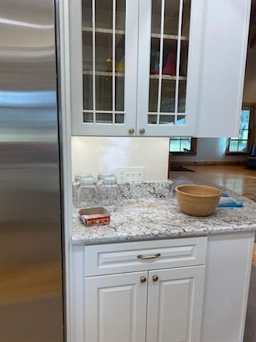 White kitchen cabinets with glass-front uppers, granite countertop, and a stainless steel refrigerator.