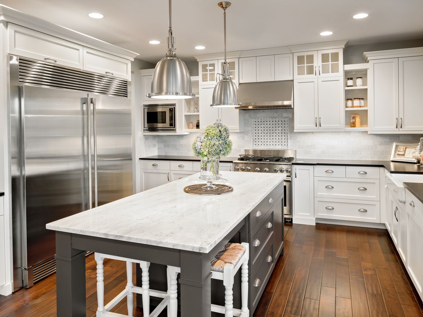 Modern white kitchen with stainless steel appliances, dark island, and pendant lights.