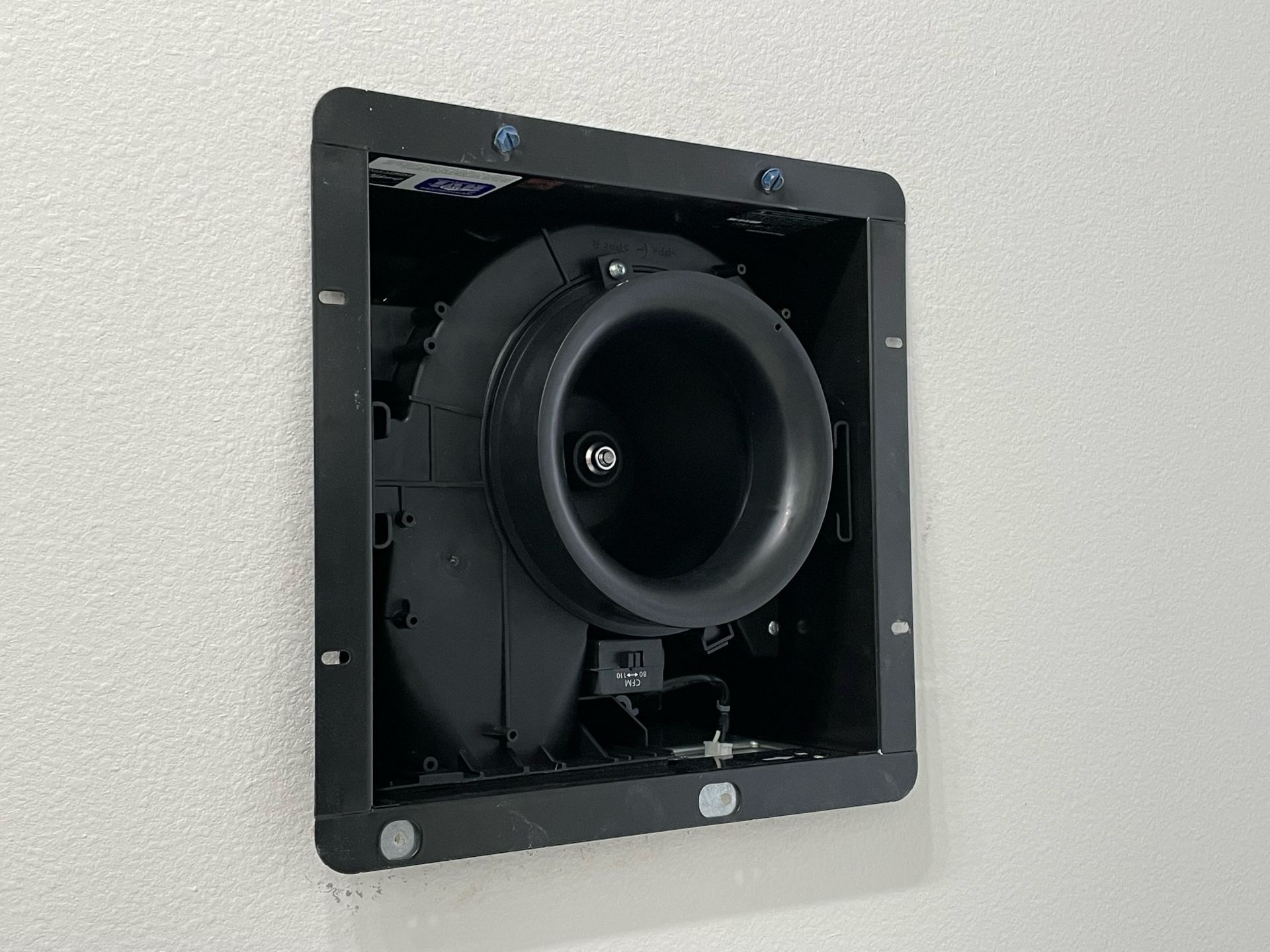 Black bathroom exhaust fan installed in a white wall.