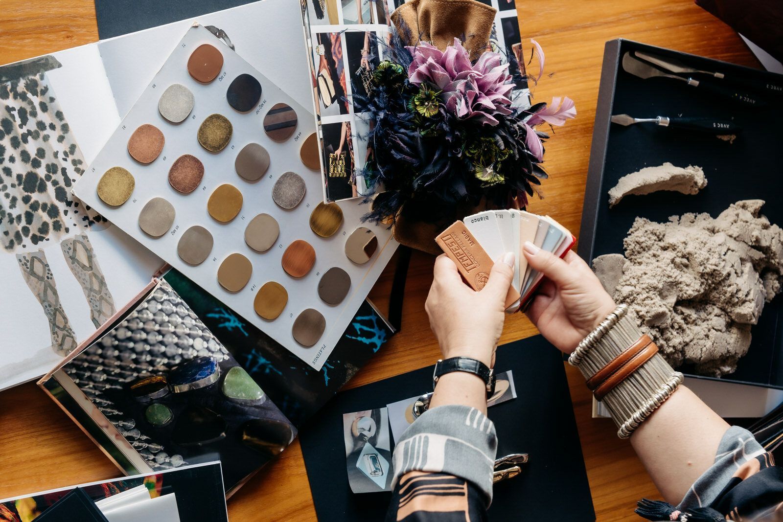 Woman comparing color swatches, surrounded by fabric samples, a floral arrangement, and design materials.