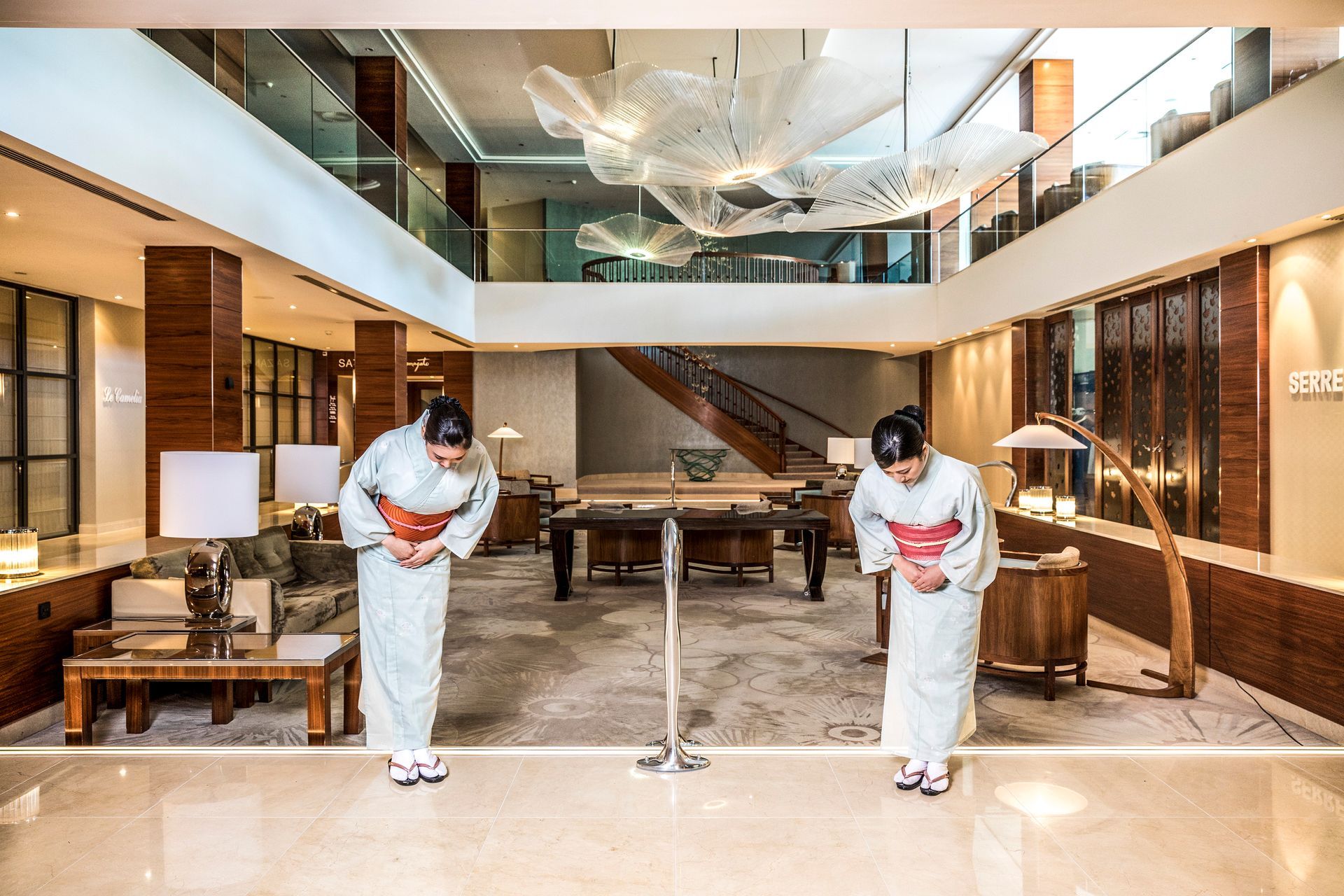 Two people in traditional Japanese attire bow in a hotel lobby.