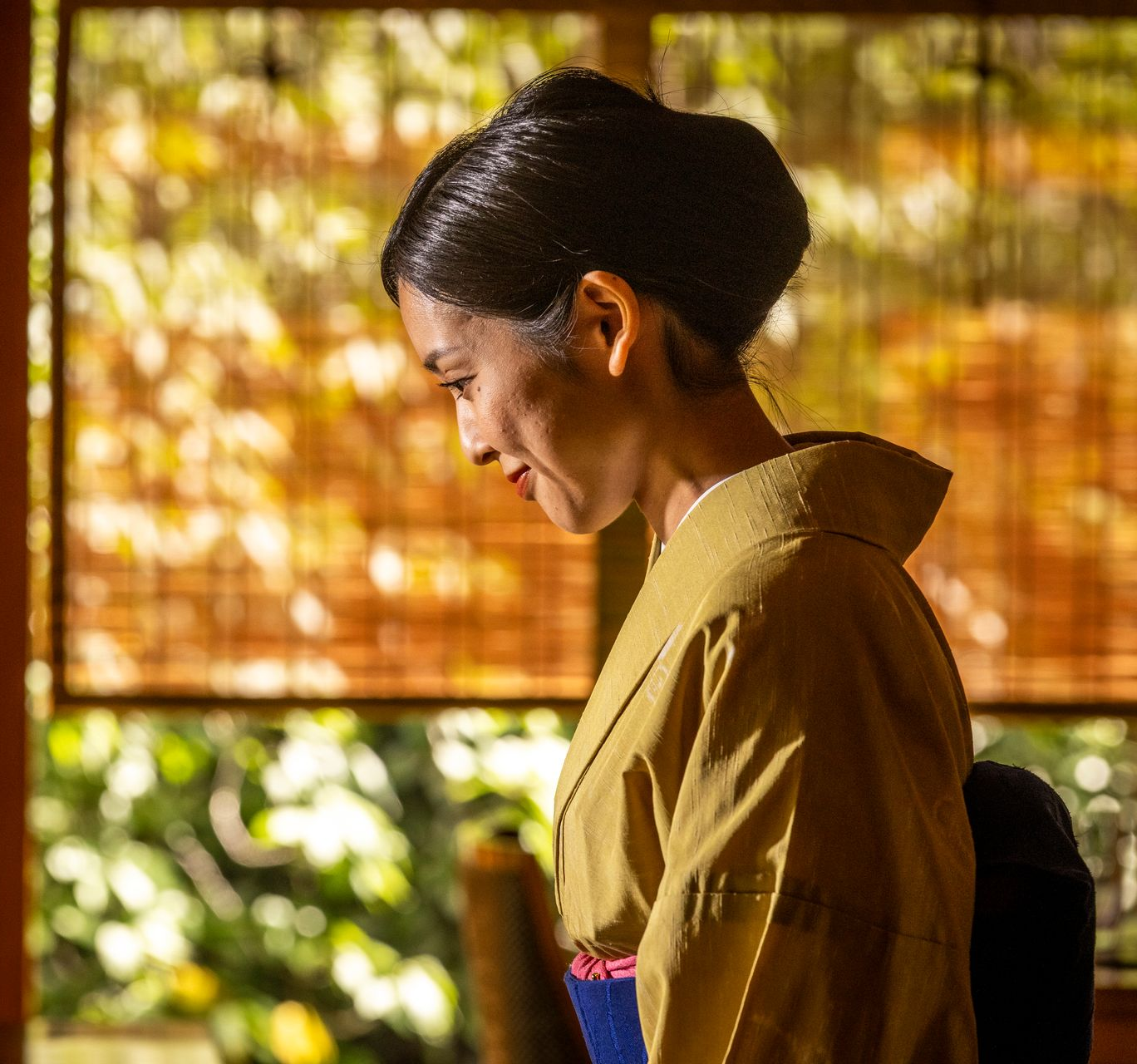 Woman in a kimono bows in front of a window, soft light shining.