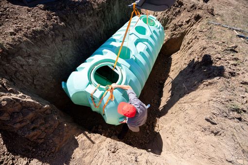 Black plastic septic tank installed in a dirt trench outdoors, with pipes visible above it