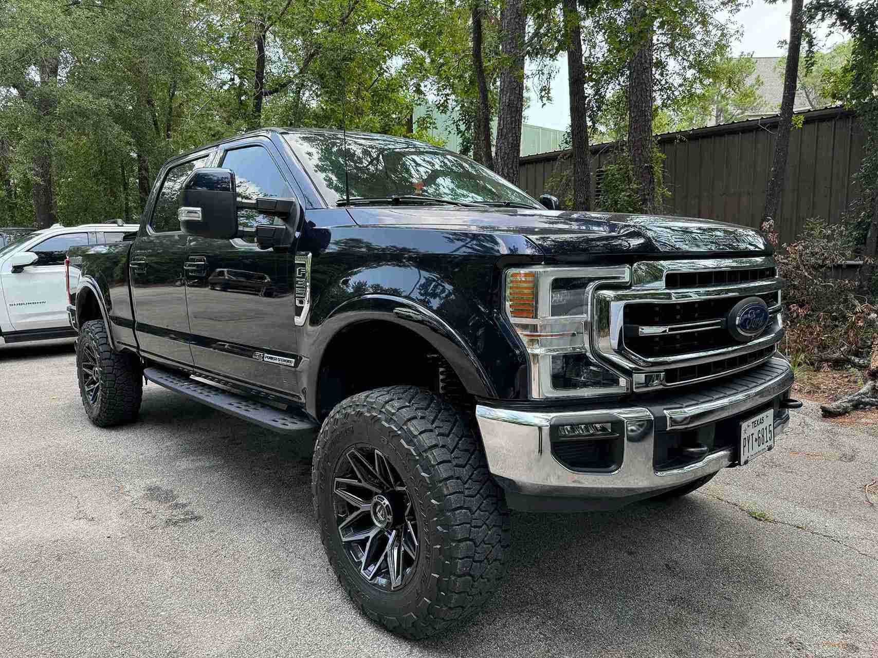 Black lifted Ford pickup truck parked on a gravel driveway with trees in the background