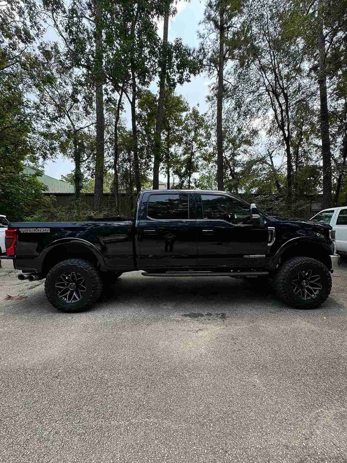 Black lifted pickup truck parked on gravel with trees in the background.