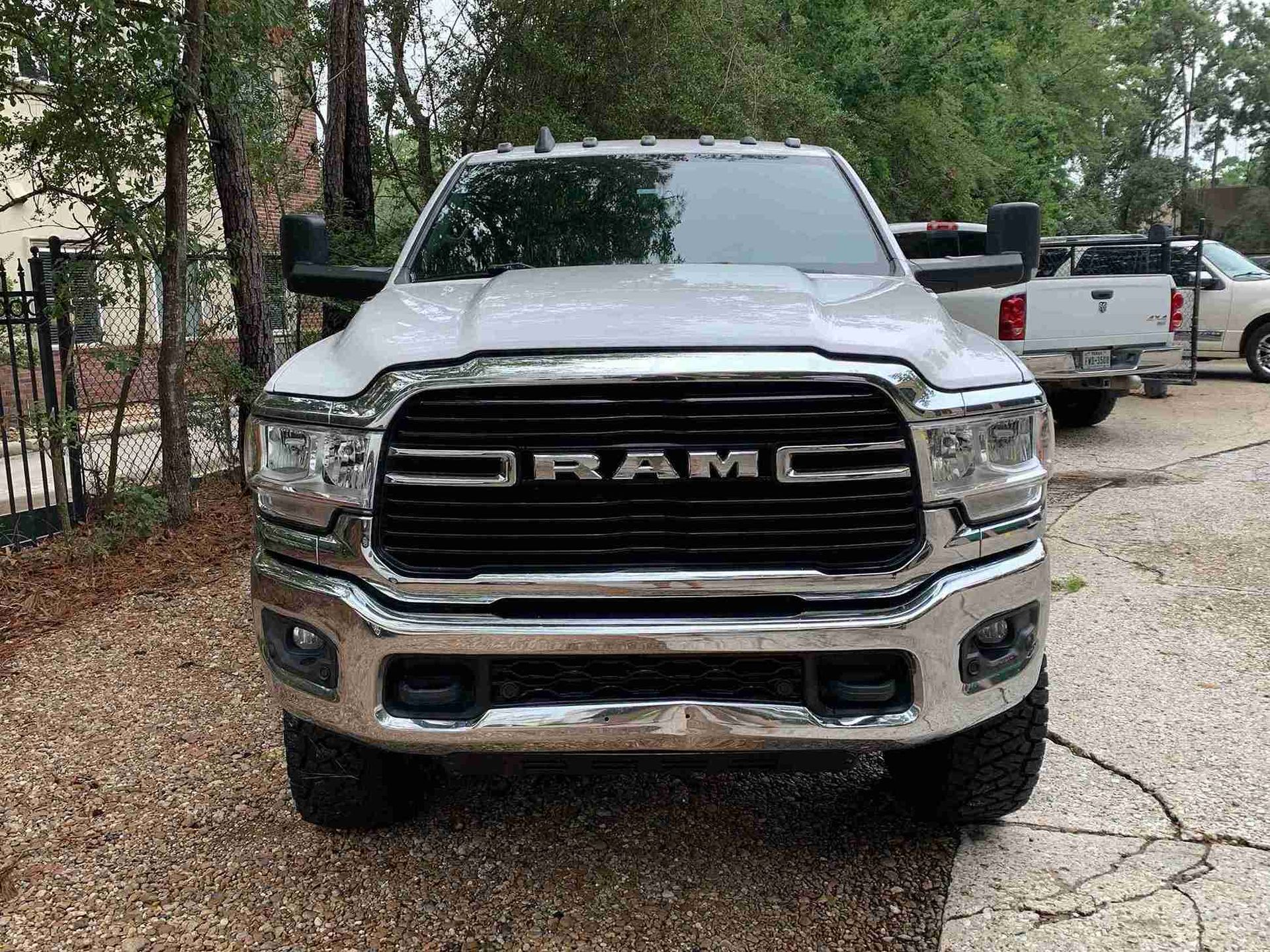 Silver RAM pickup truck parked on a wooded gravel driveway, front view