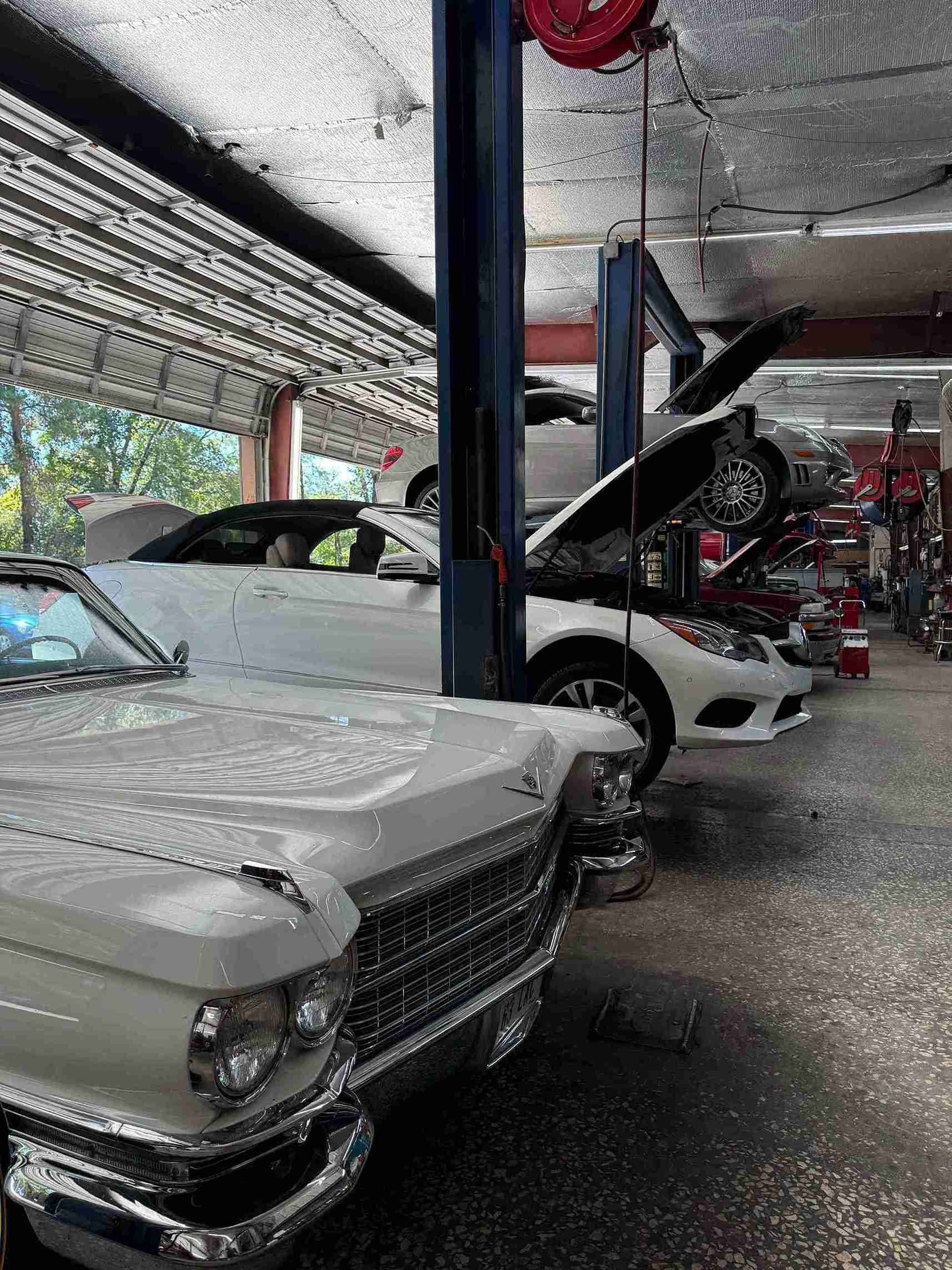 Row of classic cars in a covered garage, including a silver convertible with its hood open.
