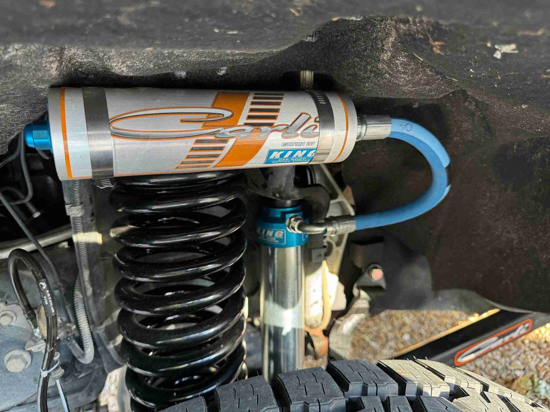 Close-up of a vehicle suspension coilover shock with blue hose and silver reservoir under the wheel well