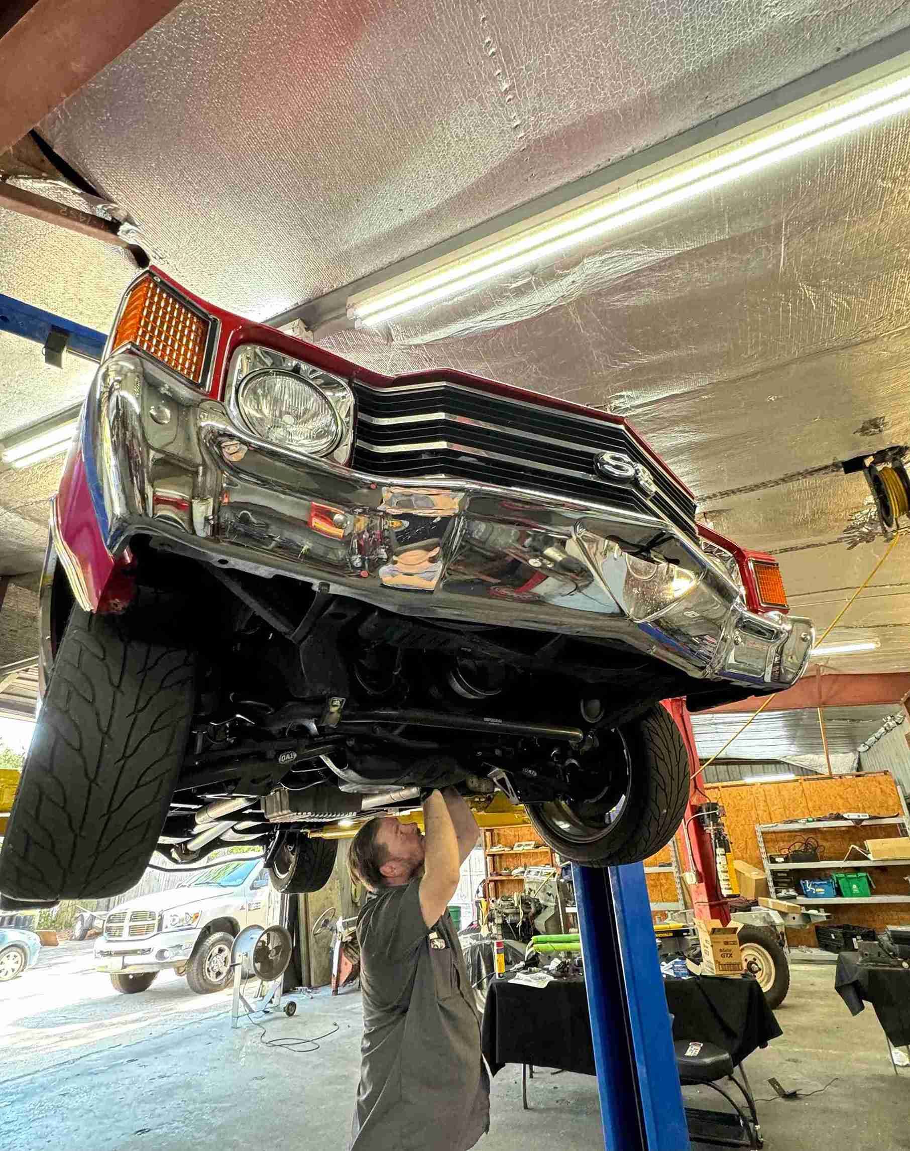 Car suspended on a lift in a workshop, mechanic working underneath the front bumper
