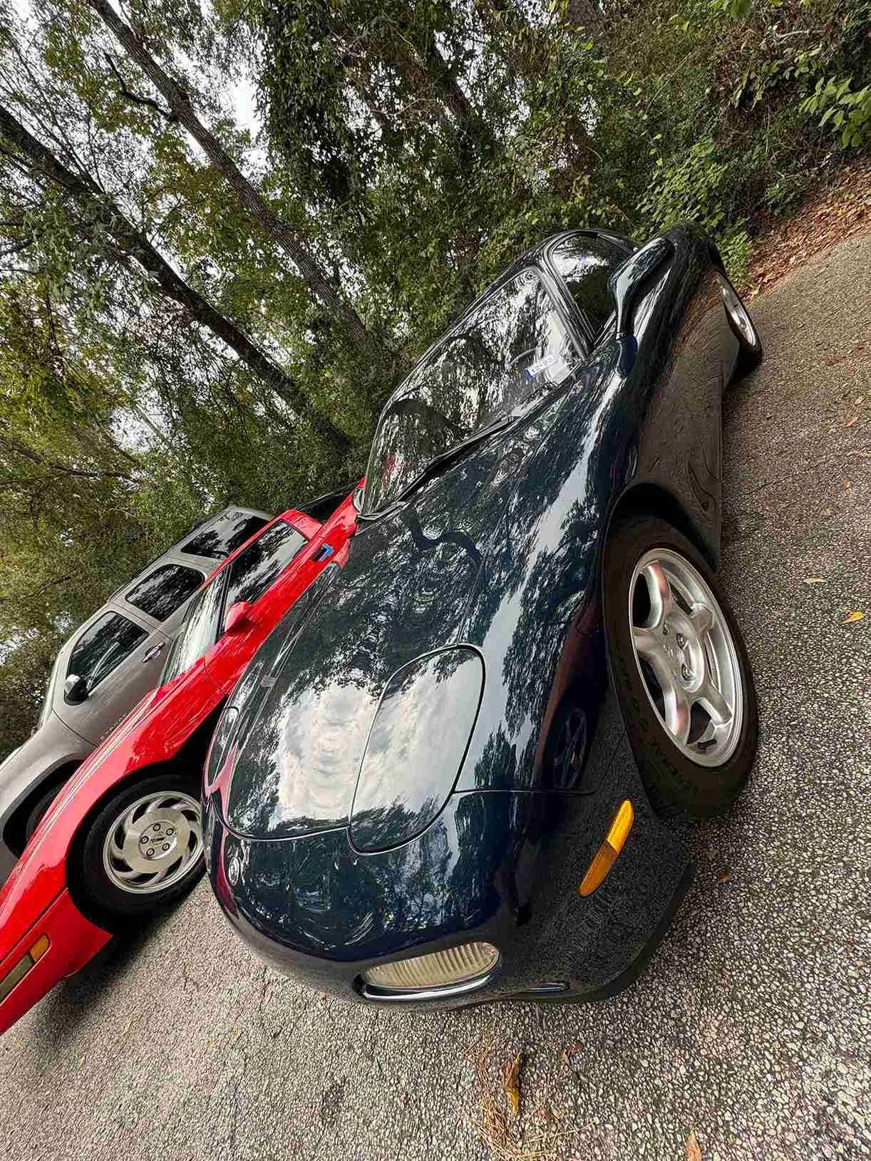 Three parked cars under trees, with a black car in the foreground and a red car beside it.