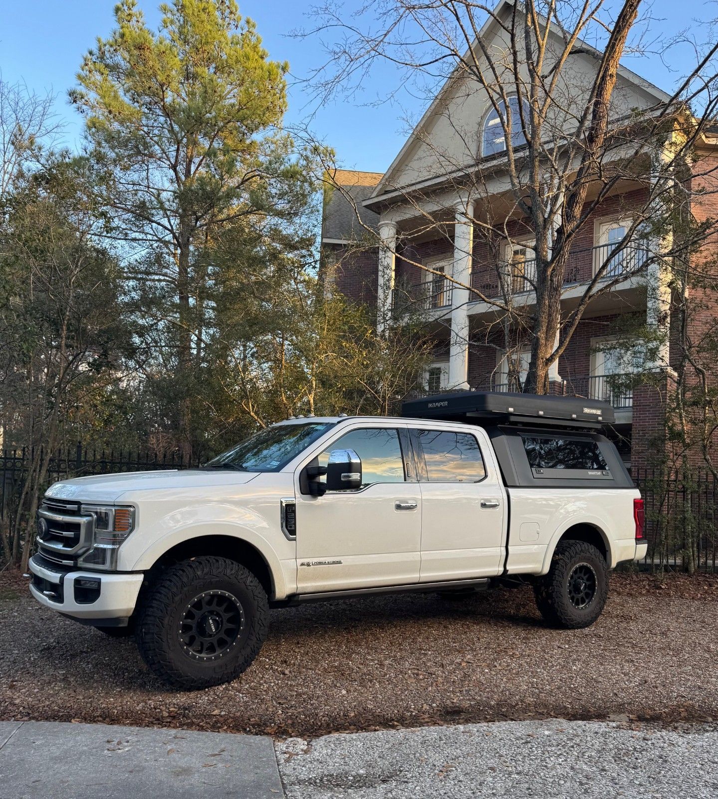 White pickup truck parked in front of a large house with white columns and trees in the yard