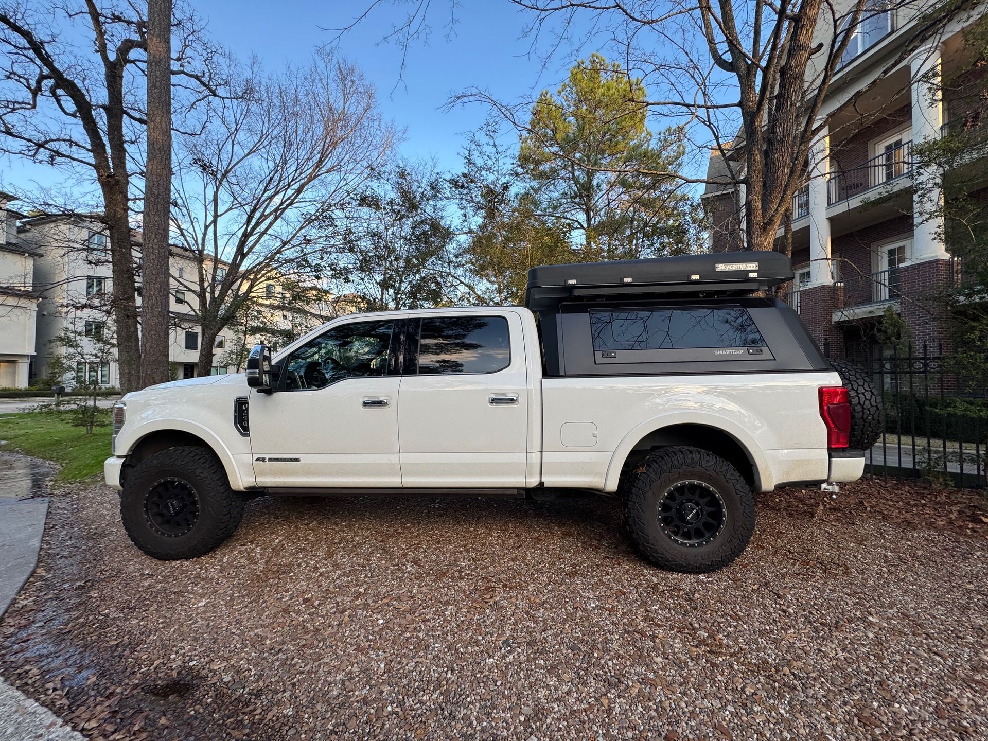 White pickup truck with camper shell parked on a leaf-covered residential street