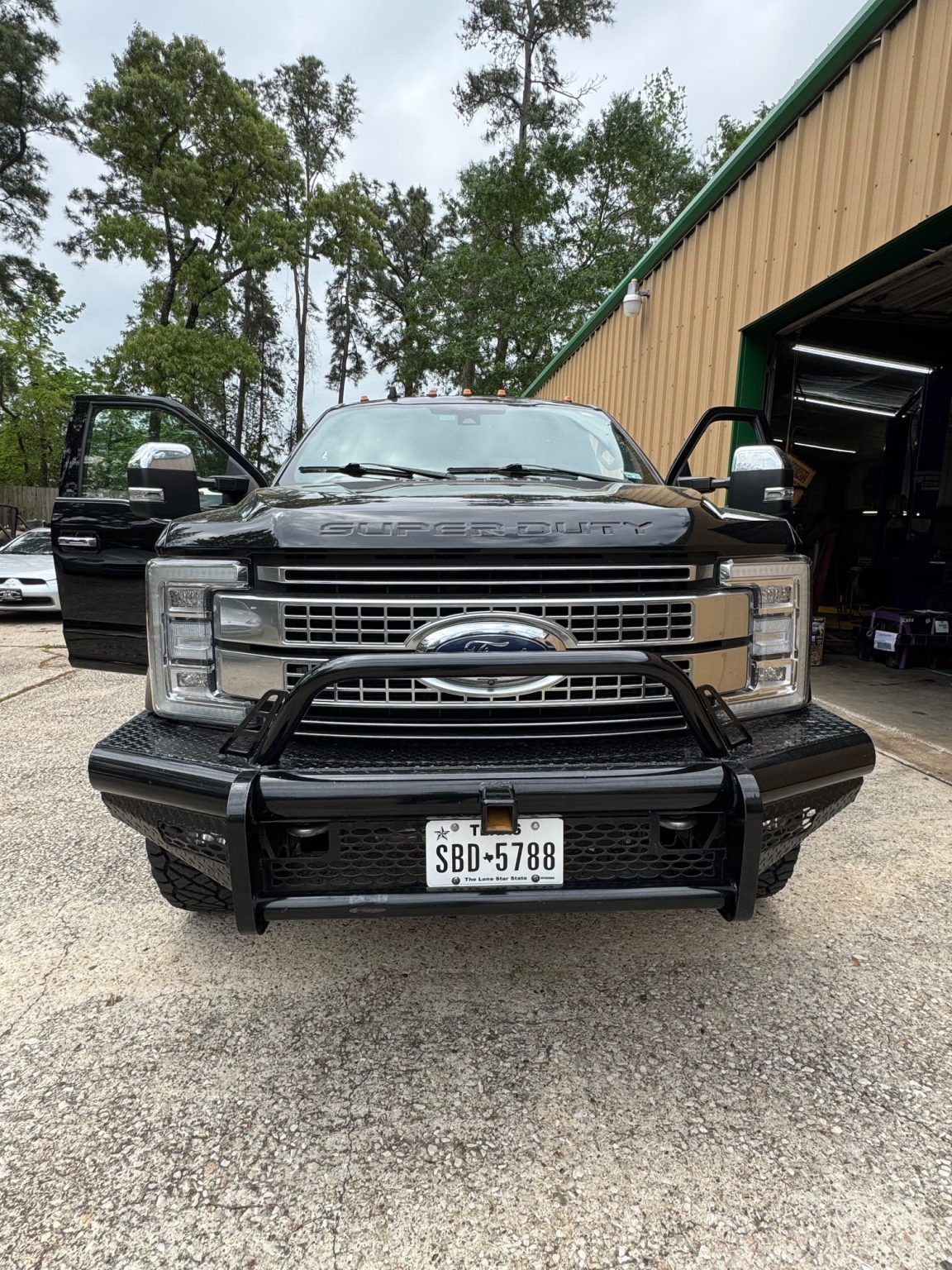 Black Ford truck facing forward outside a garage, with doors open and a building in the background