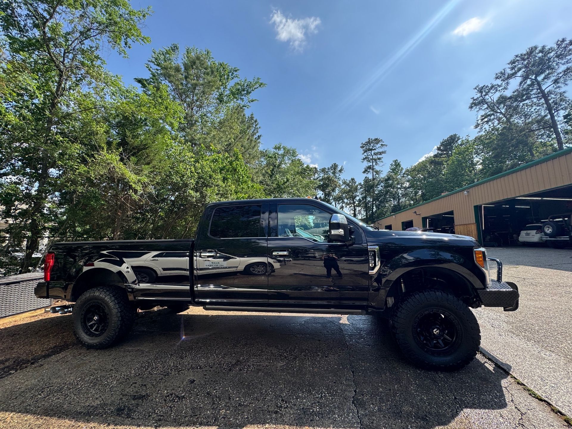 Black lifted pickup truck parked on gravel beside a garage under a bright blue sky