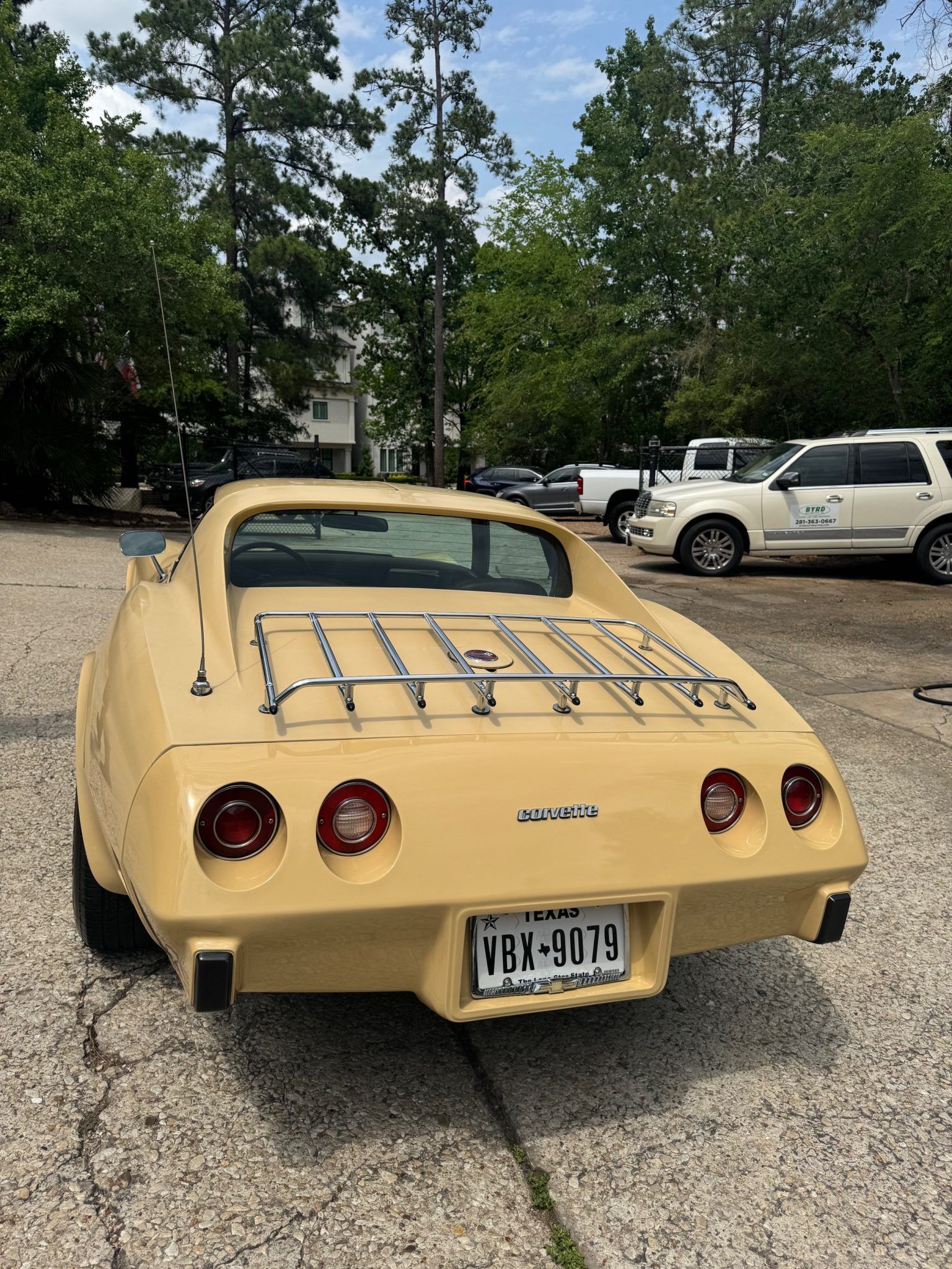 Beige vintage sports car parked in a lot with trees and other vehicles behind it.