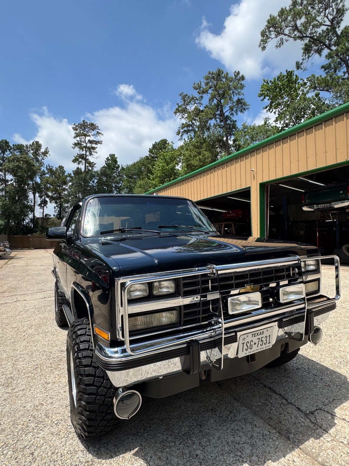 Black lifted pickup truck with chrome grille parked outside a garage under a sunny sky