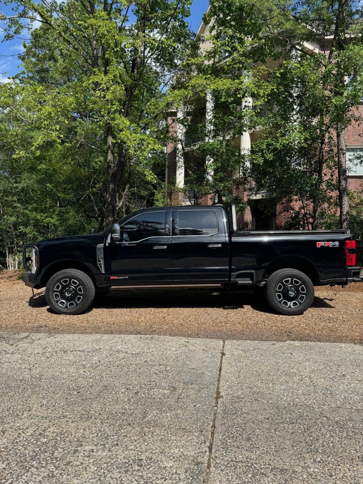 Black pickup truck parked beside a wooded apartment building on a sunny day