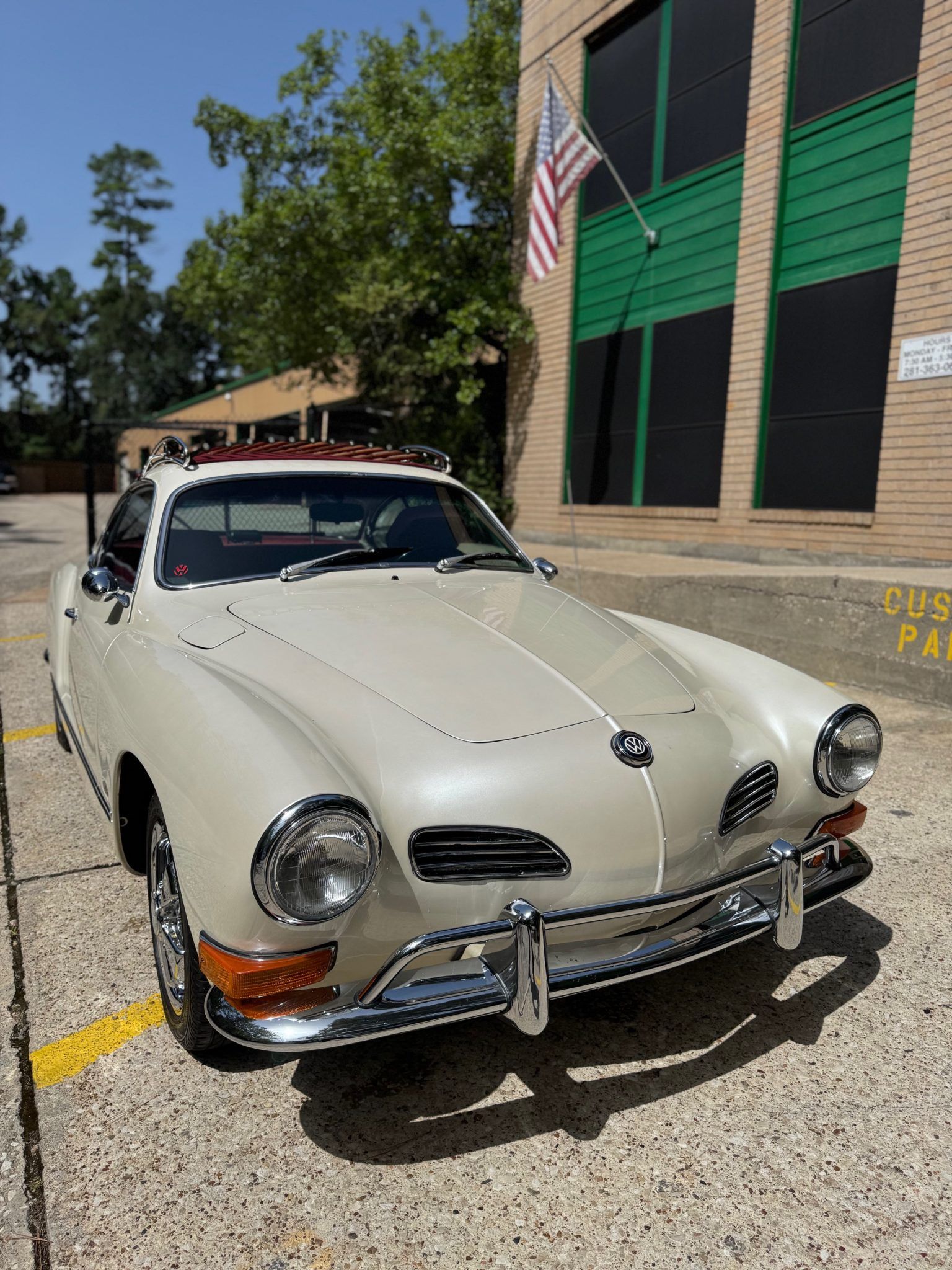 Vintage beige convertible car parked outside a building with an American flag.