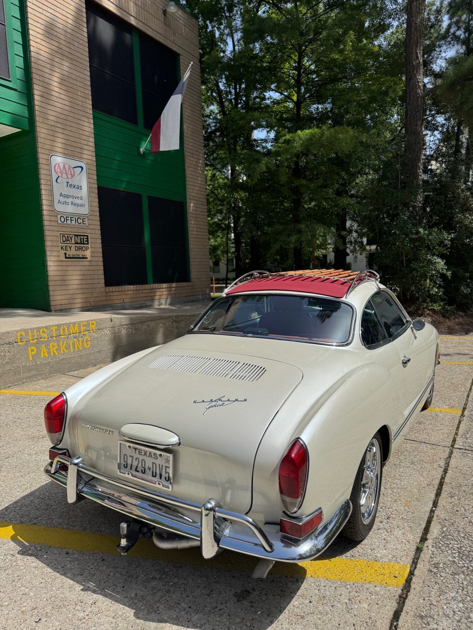 Vintage cream convertible parked beside a building, with a red roof and chrome bumper.