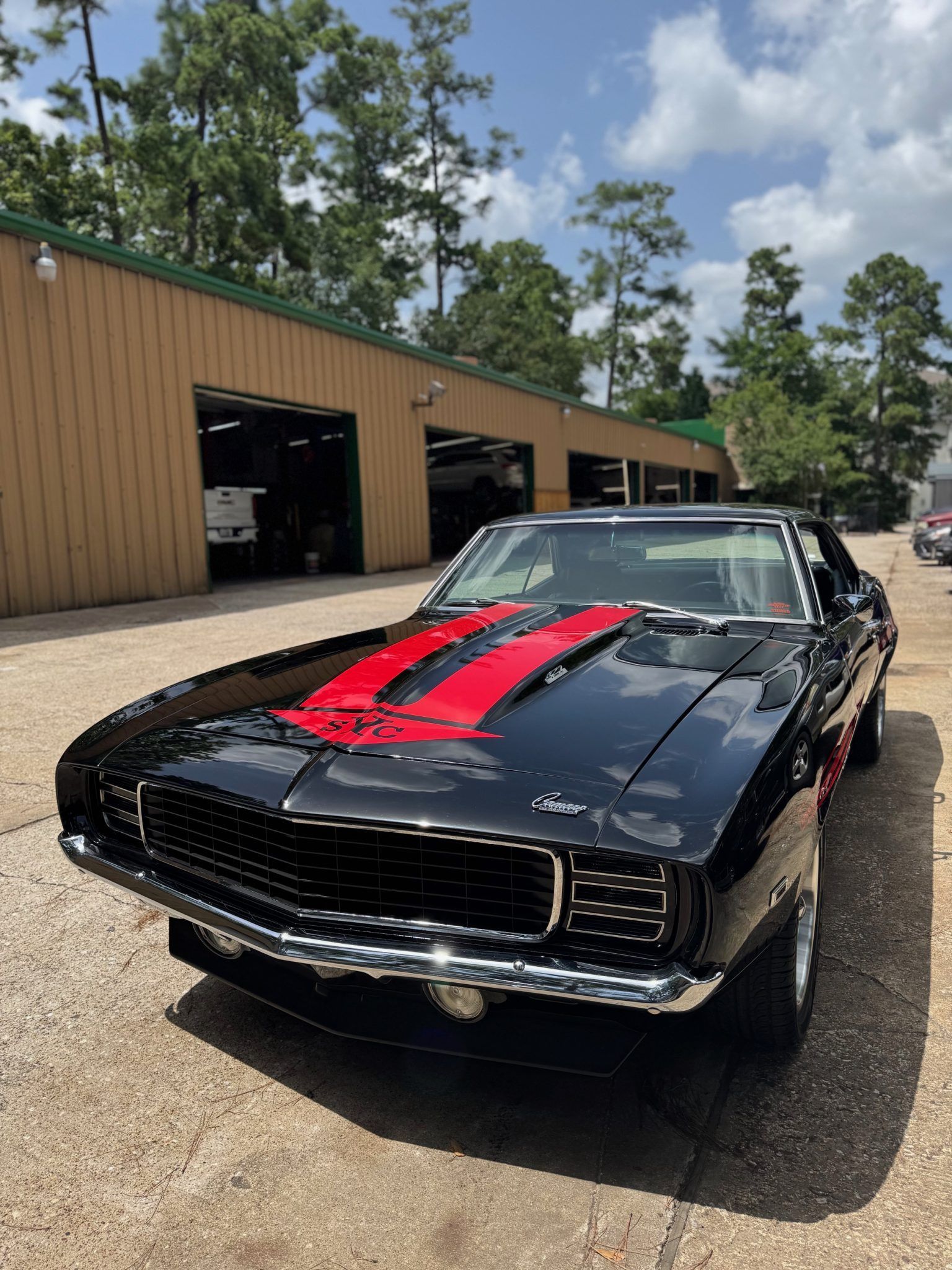 Black classic muscle car with red racing stripes parked outside a garage.