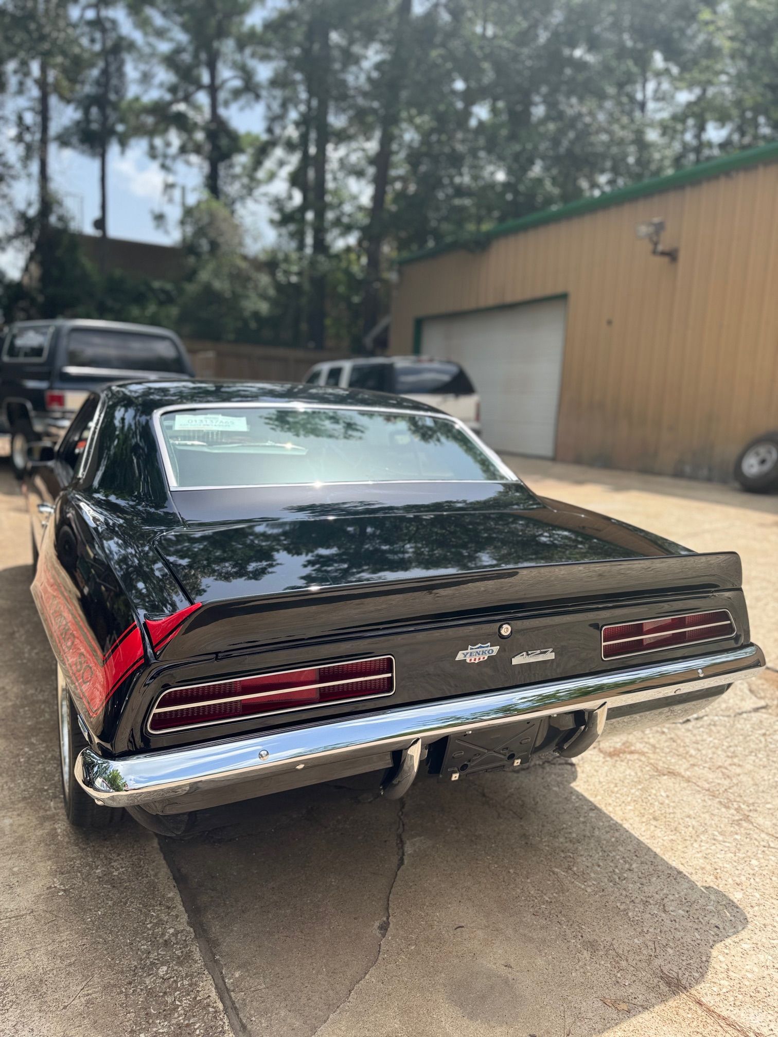 Black classic car rear view with chrome bumper, parked outdoors beside a tan garage.