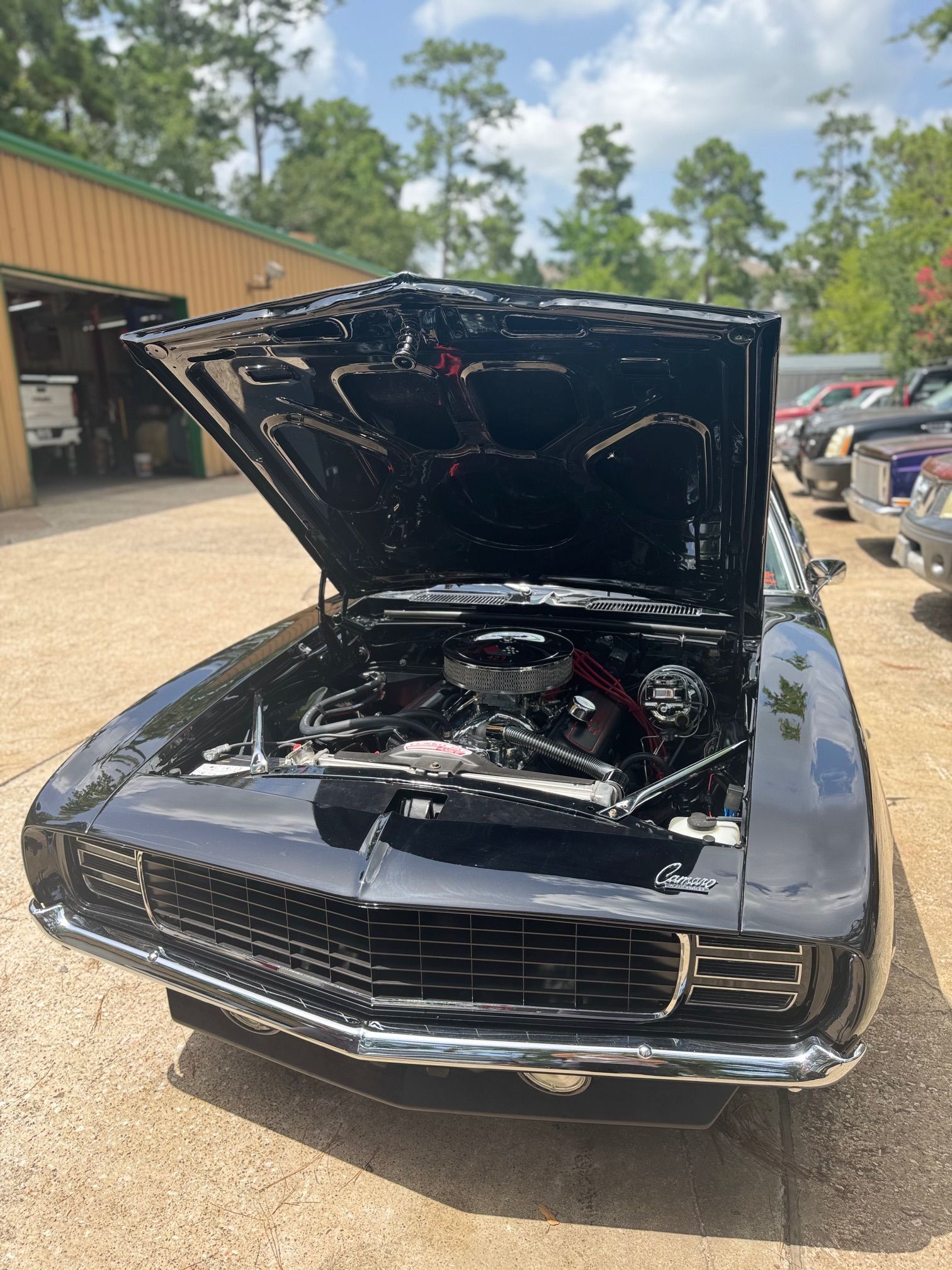 Black classic car with hood open in a parking lot, showing engine bay.