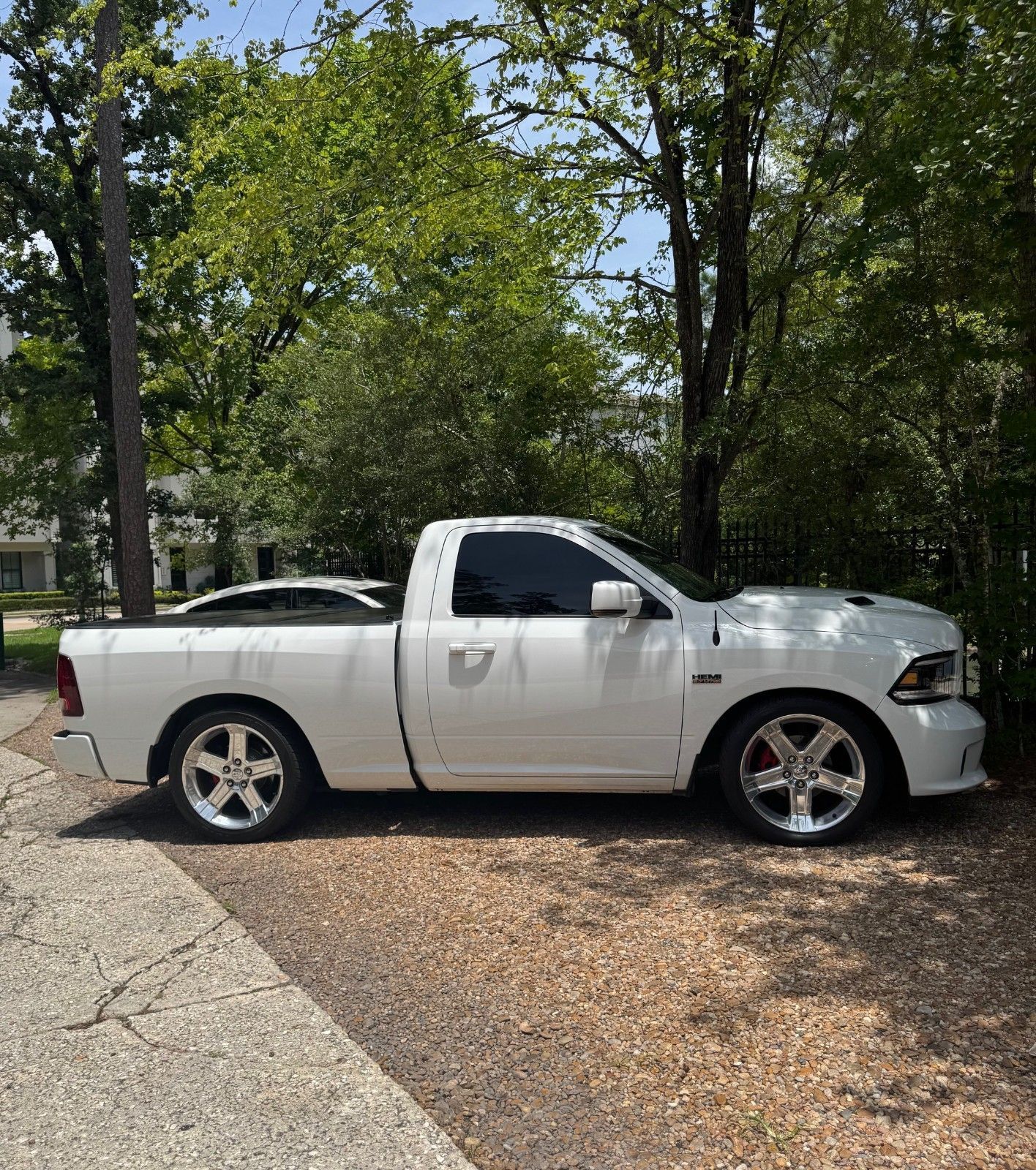 White pickup truck parked on a gravel driveway surrounded by trees and greenery