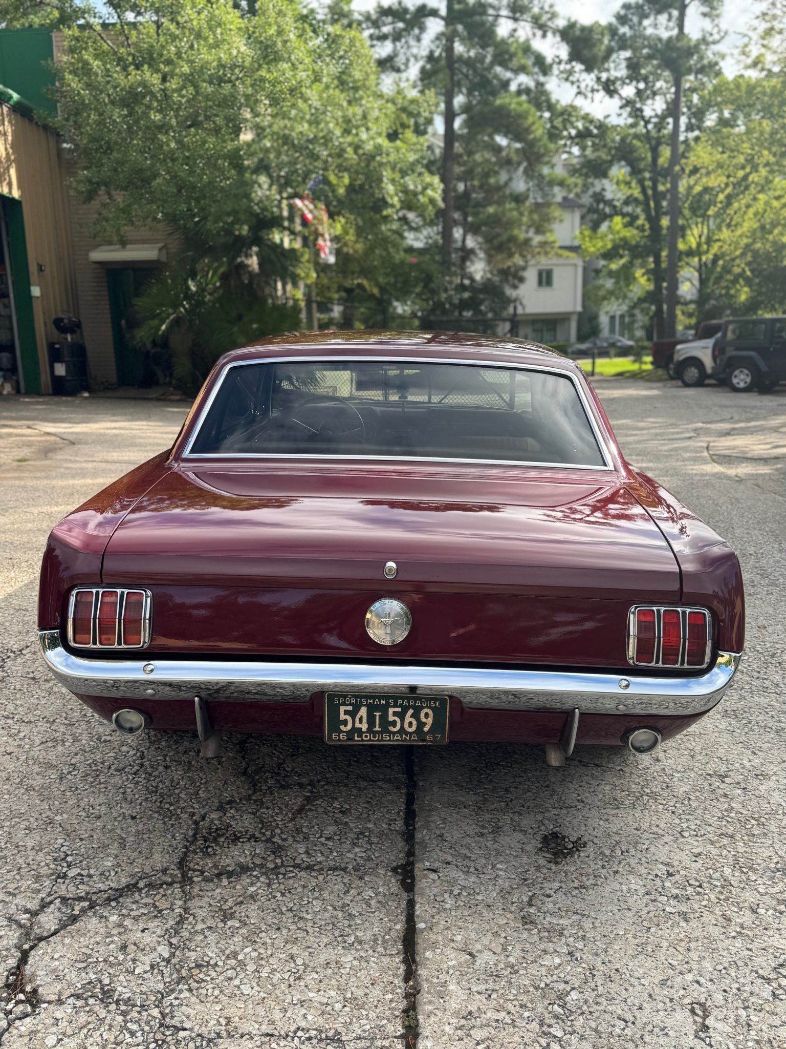 Rear view of a burgundy classic car parked on a gravel driveway under trees