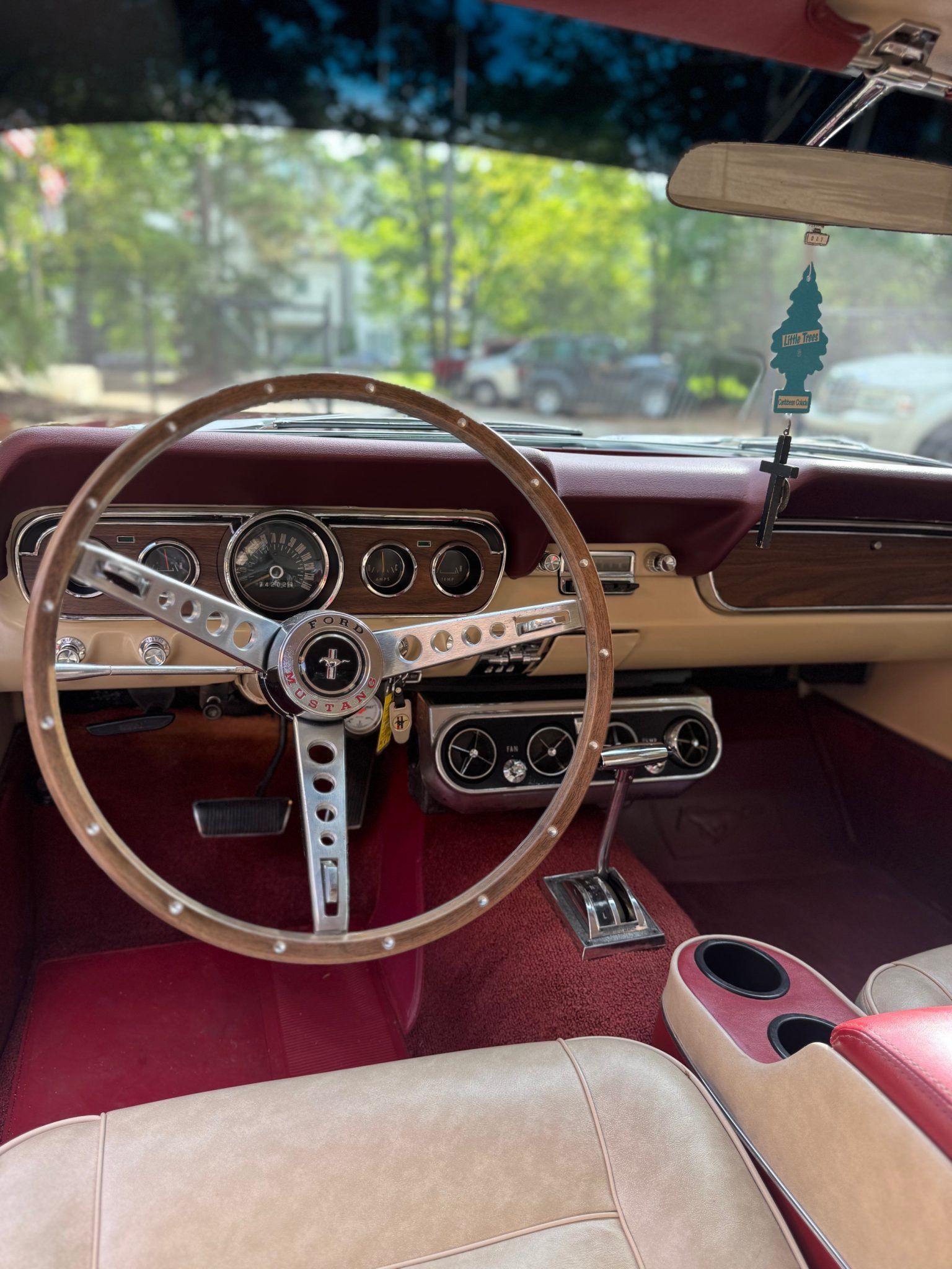 Vintage car interior with burgundy dashboard, wood steering wheel, and beige seats seen through the windshield