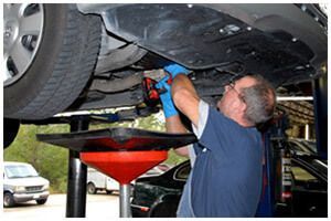 Mechanic using a power tool under a car on a lift in an auto repair shop
